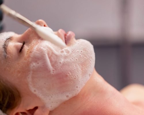 close-up beautician in gloves applies foam with a brush to the client’s face takes care of the skin close-up beautician in gloves applies foam with a brush to the client's face takes care of skin